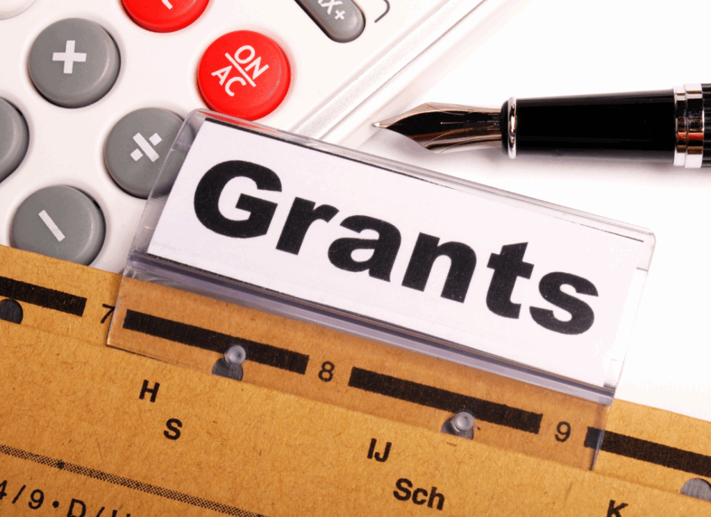A close-up of a file folder labeled "Grants" sits next to a calculator and fountain pen, symbolizing organized financial tracking for effective nonprofit grant management.